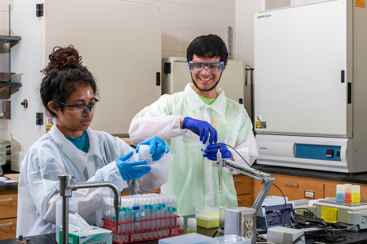 Students working in a lab with lab coats and safety equipment
