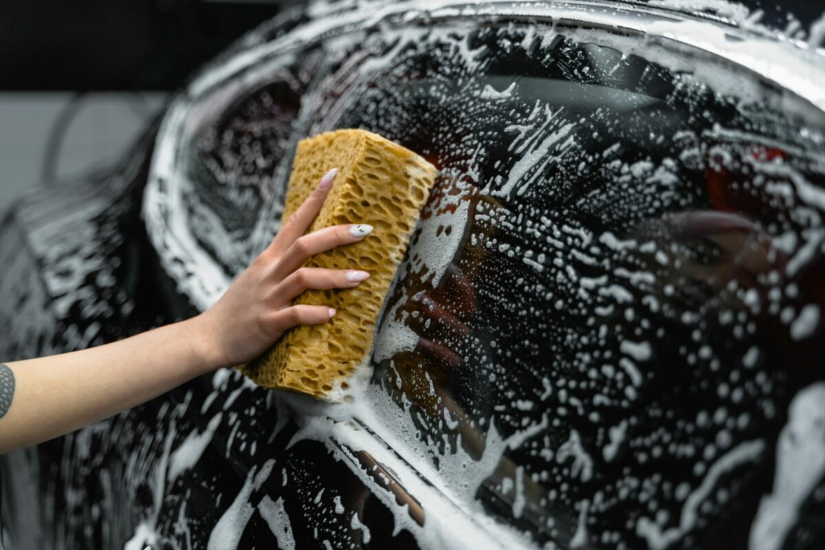 Sponge with hand wiping a window of a car