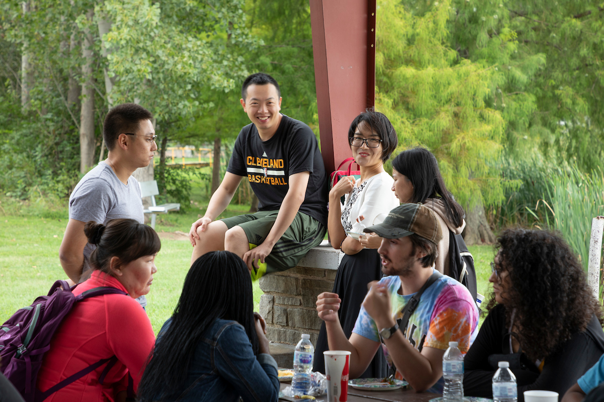 A group of students have a conversation at a pavilion in a park.