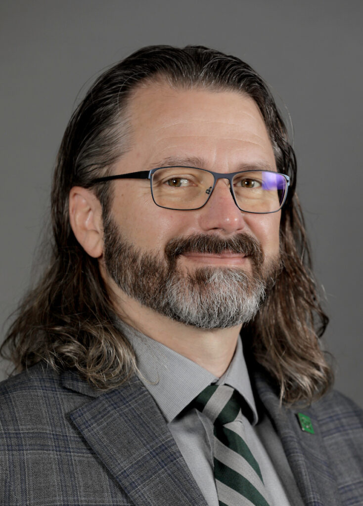 A man with glasses, a beard wearing a suite with tie.