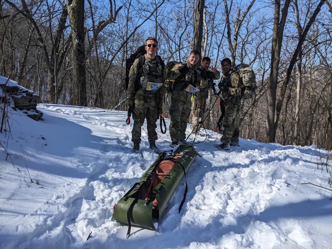 Men in uniform with a sled in the snow.