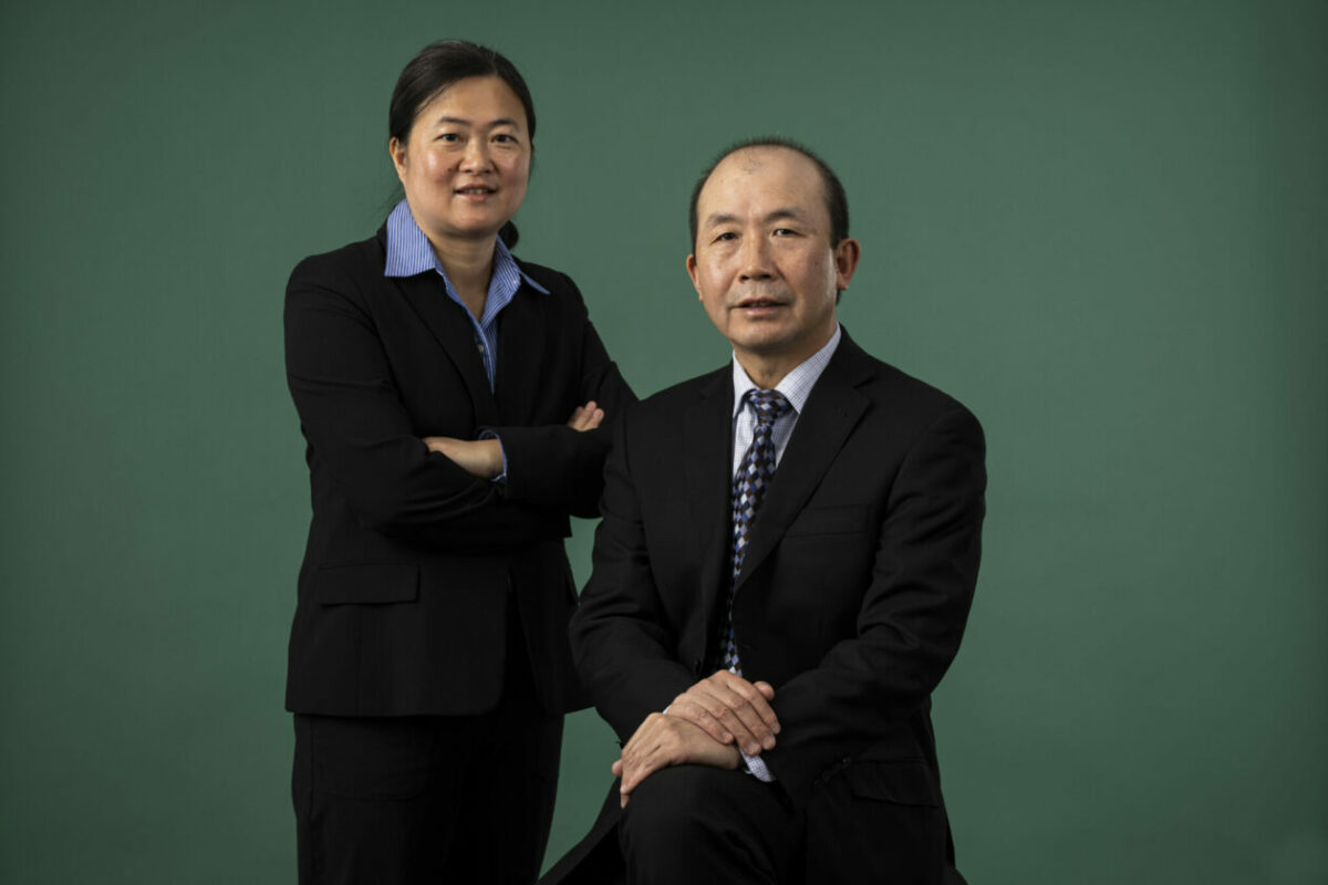 Two people wearing suits posing in front of a green background.