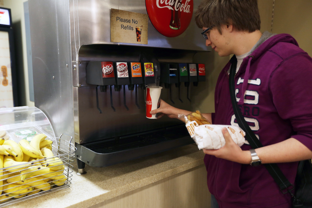 Student filling cup at a soda machine.