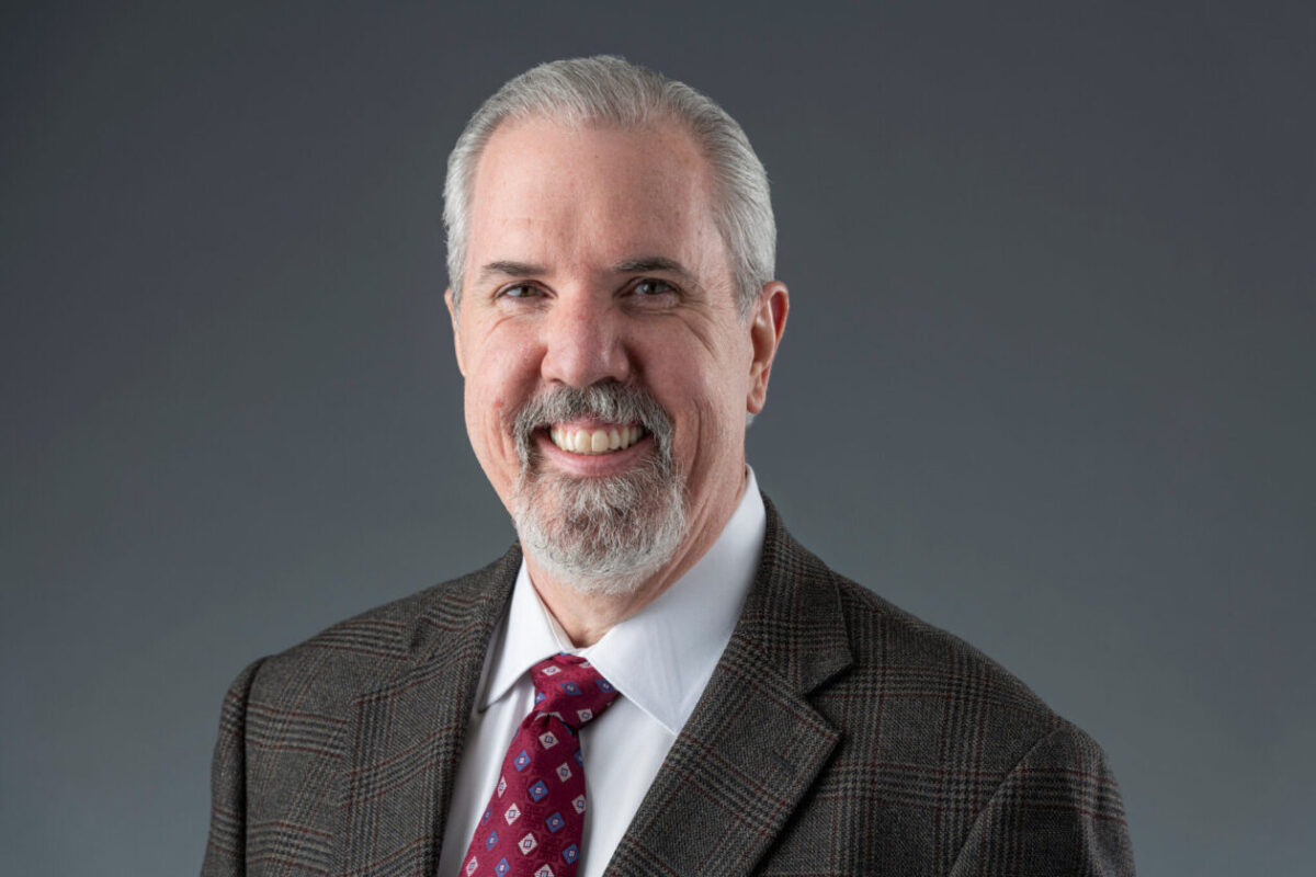 A man wearing a jacket and tie for a headshot.