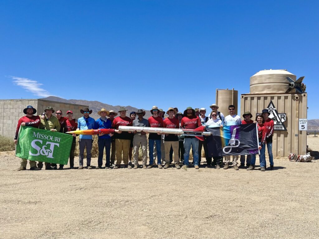 A group of students holding a rocket and a green Missouri S&T flag.