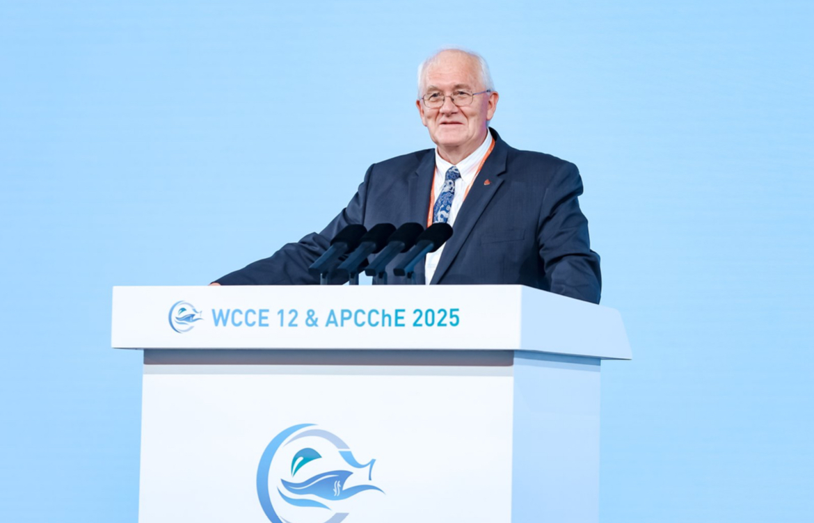 A man standing at a podium wearing a dark blue blazer and tie.