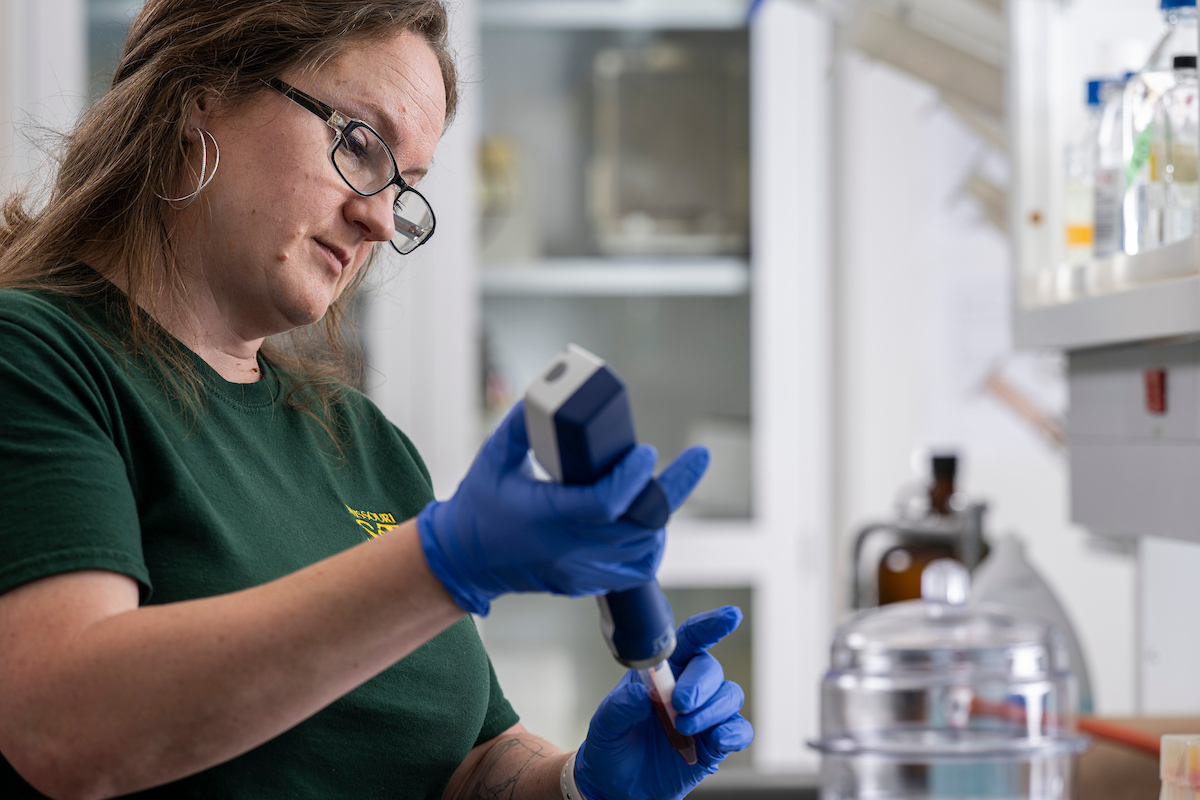 A woman wearing glasses and safety gloves works in a laboratory.