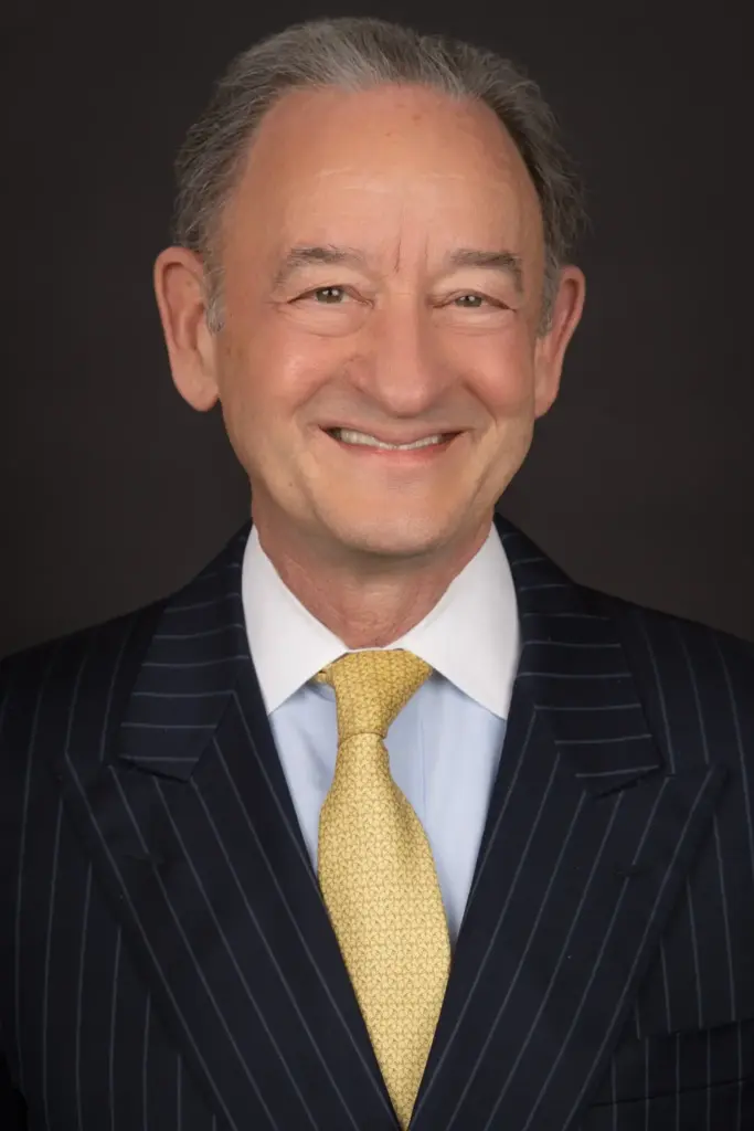 A professional headshot of Dr. Mark Wrighton wearing a pinstriped black suit jacket with a gold tie.