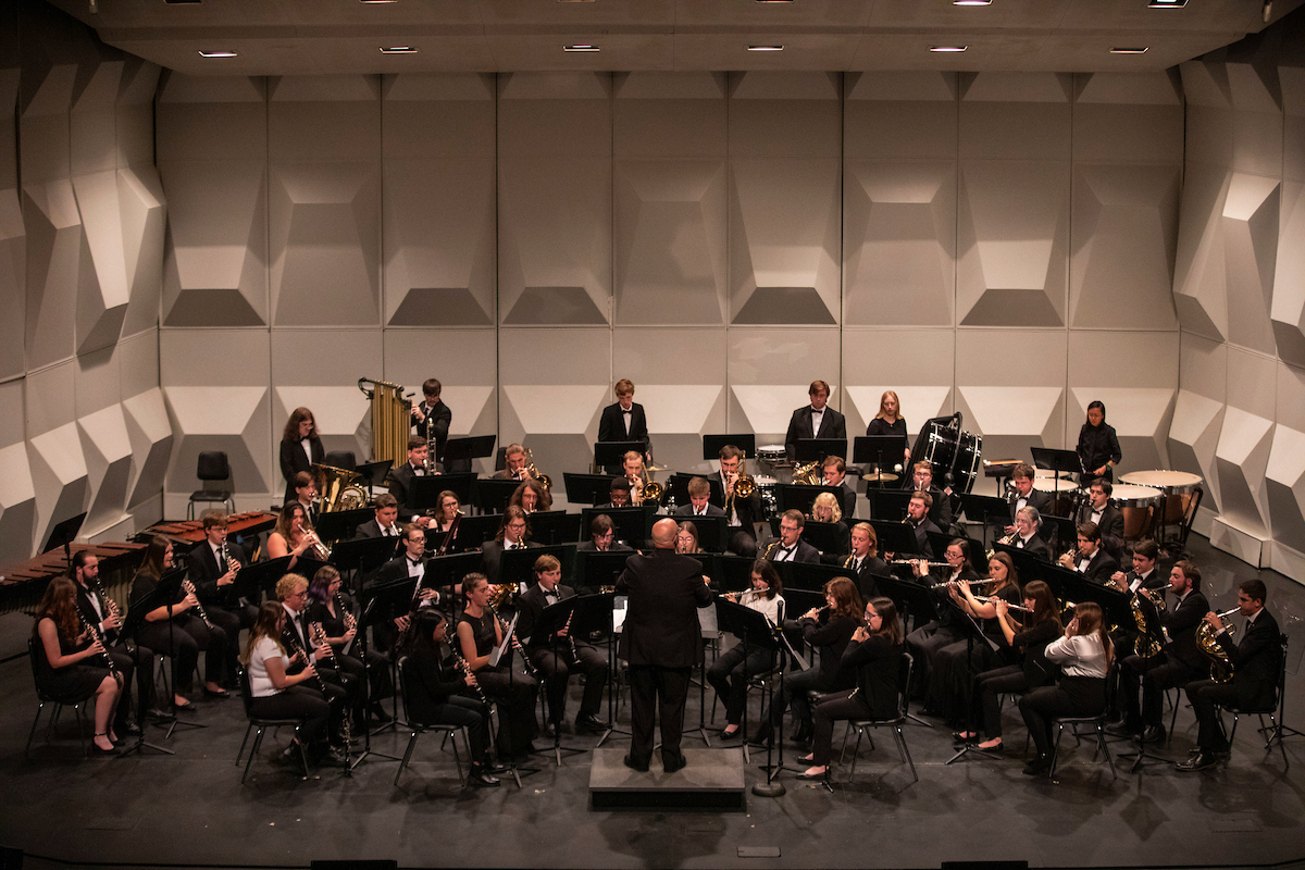 The wind symphony sits in three curved rows with a director at the podium.