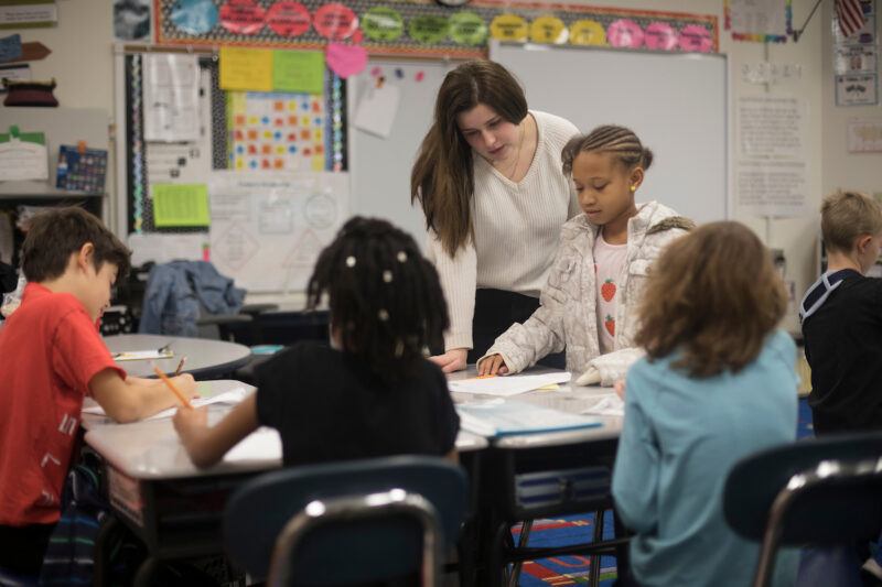 A woman helps grade school students in a classroom.