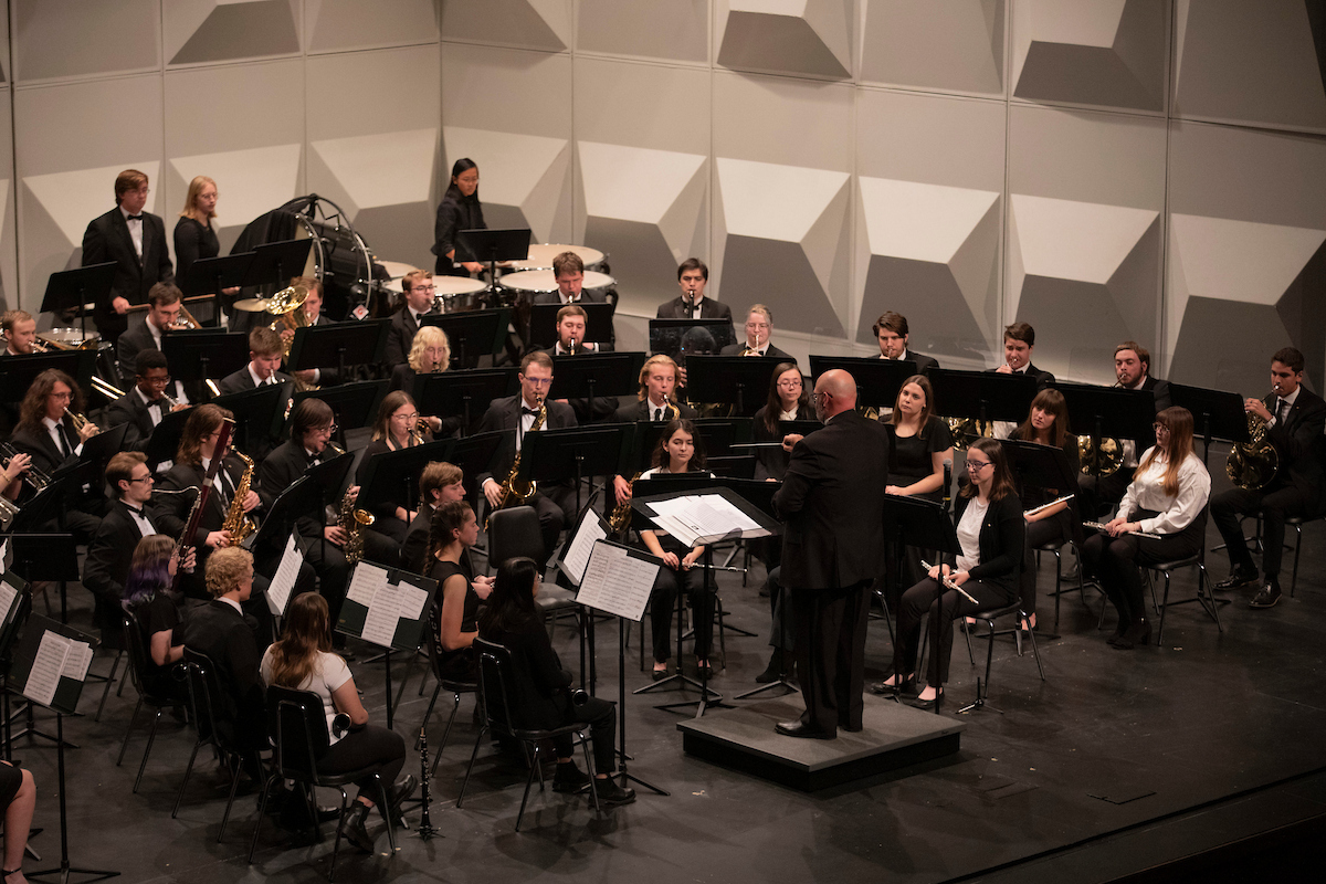 A wind symphony on a stage playing music with a director in front.