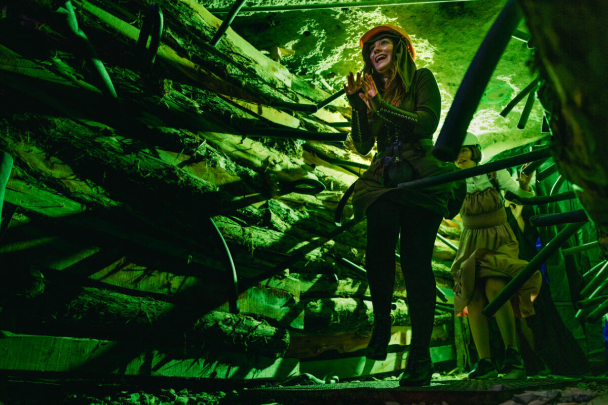 A woman walks through the haunted mine wearing a hard hat.