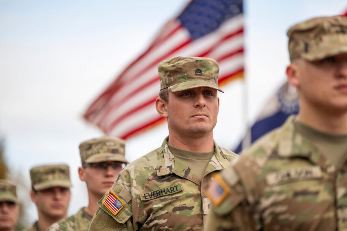 Men in ROTC uniforms with an American flag behind them.
