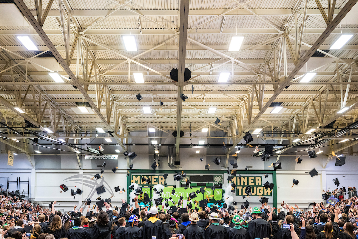 A gym full of graduates throwing their hats into the air.