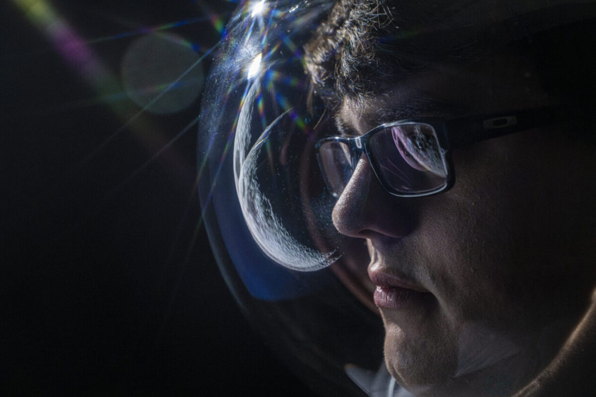A side profile of Jacob Ortega with a reflection of the moon in the image and in his glasses.