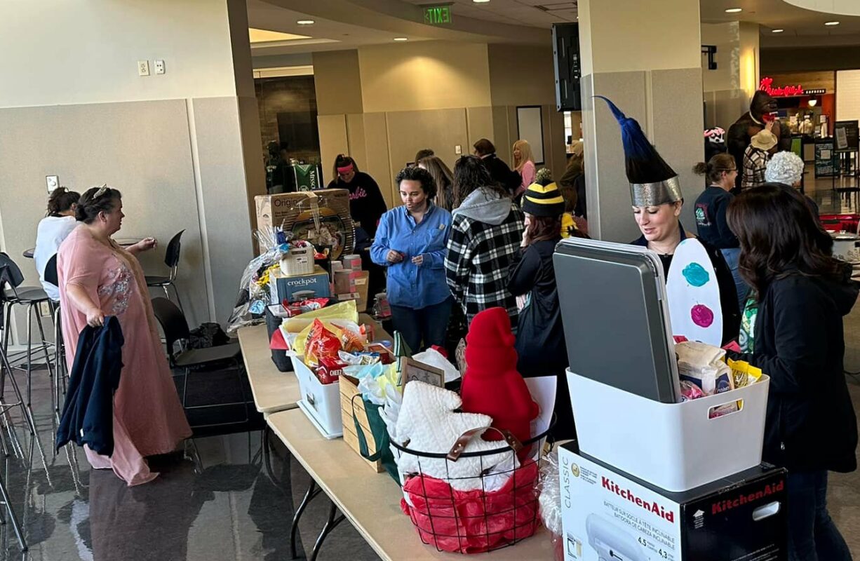 Staff members dressed in costume look at raffle baskets on a table.