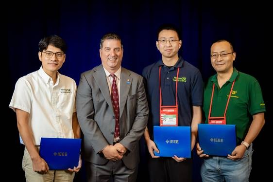 Four men stand with three of them holding IEEE folders.