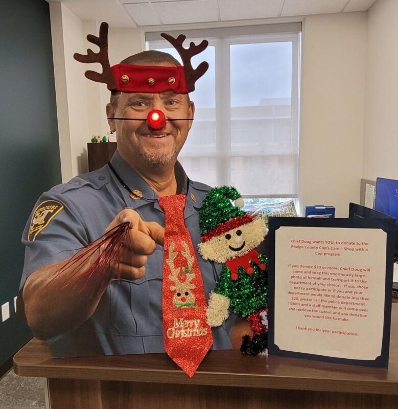 A cutout of Chief Doug Roberts with holiday decorations with a sign explaining how to donate money to the Shop with a Cop program.