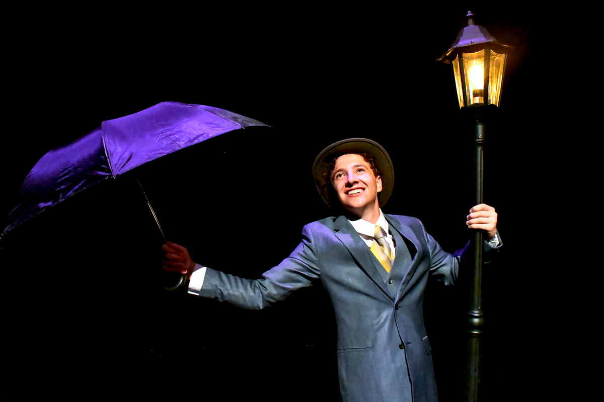 A person dancing with an umbrella holding onto a lightpole.