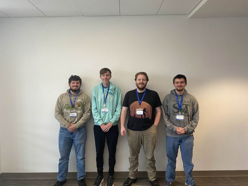 Four students stand against a wall for a photo.