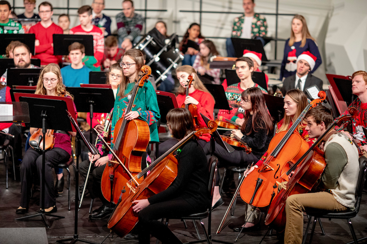 Students wear festive holiday sweaters while performing music with an array of musical instruments.