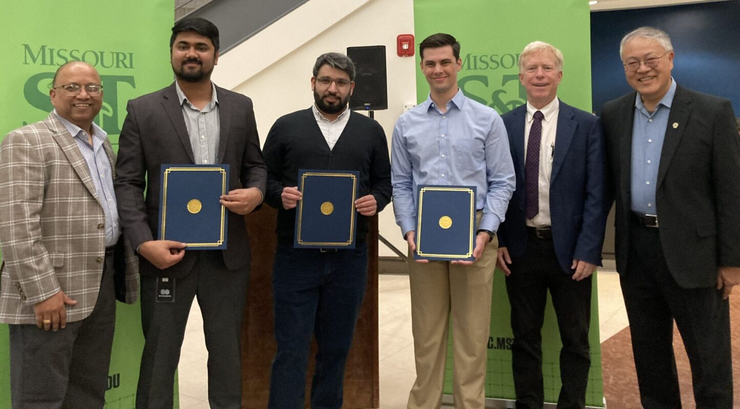 Three men hold certificate folders and pose for a photo with three other men.