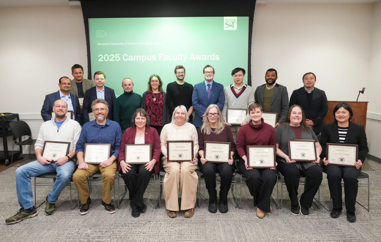 Eighteen faculty members pose for a photo with their certificates in front of a projector screen.