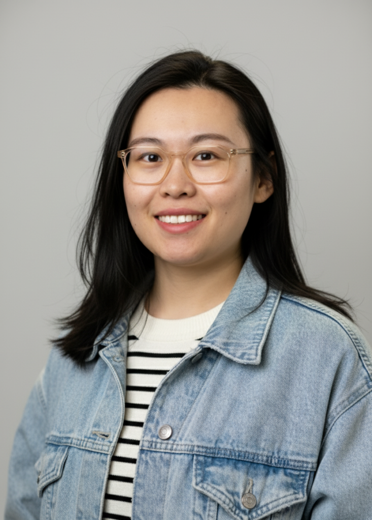 A woman wearing glasses with dark hair wearing a jean jacket with a striped sweater.