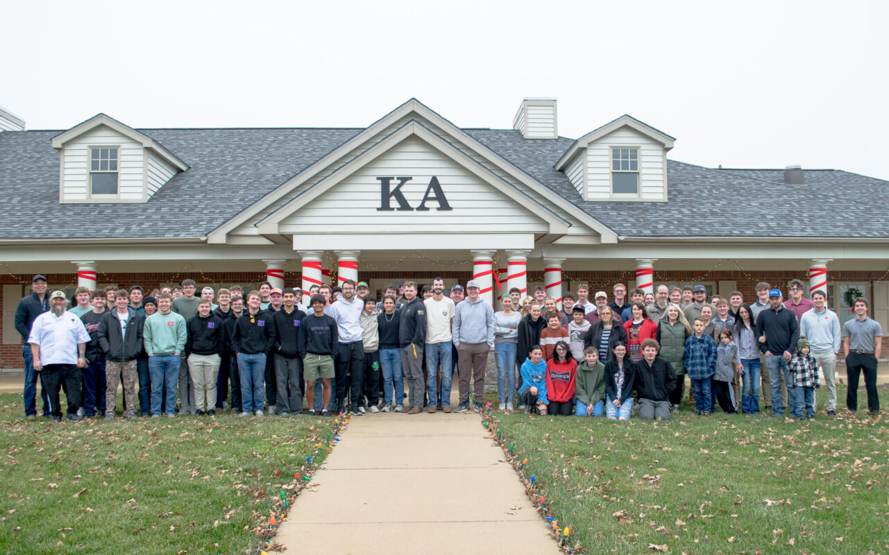 A large group of people pose for a photo in front of the Kappa Alpha house.