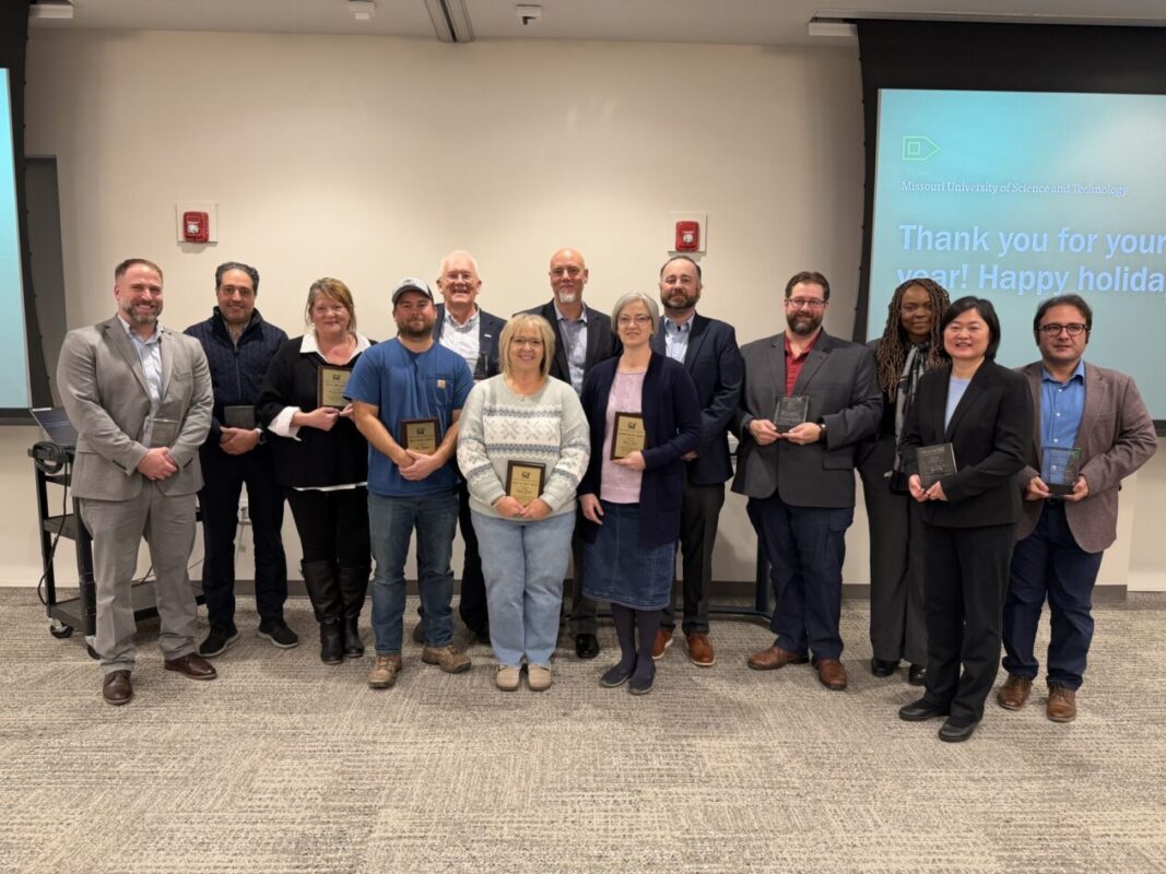 A group of people pose together for a photo - many are holding plaques.