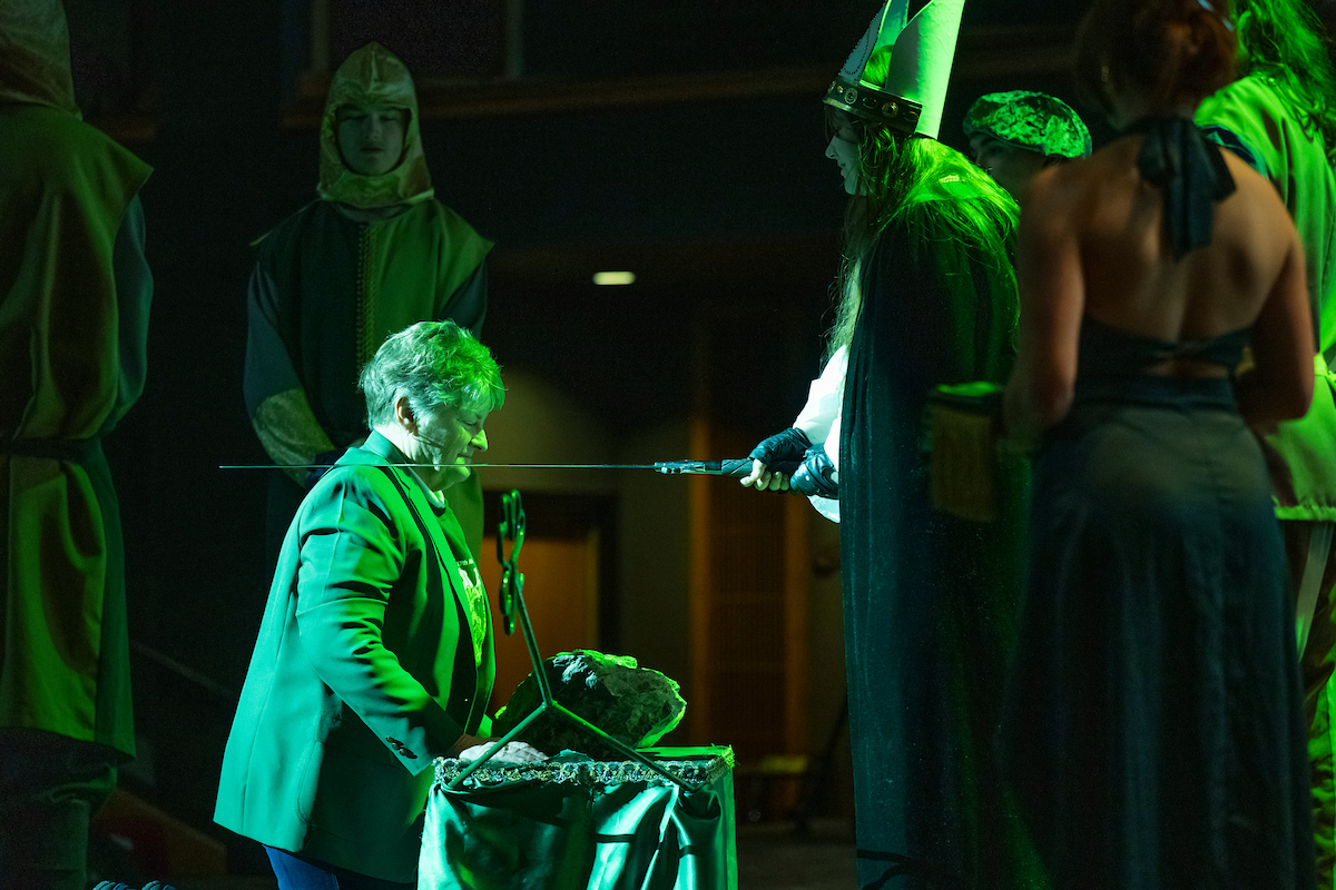 A woman wearing a green blazer kneels at the blarney stone to be knighted by St. Patrick in 2025.