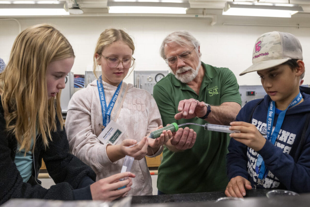 Three students wearing lanyards and a professor work with syringes and tubing to show methods to compare enhanced oil recovery.