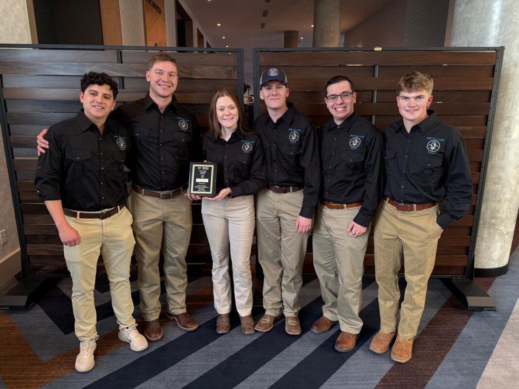 Six students wearing matching long sleeved polo shirts pose for a photo with one holding a plaque.