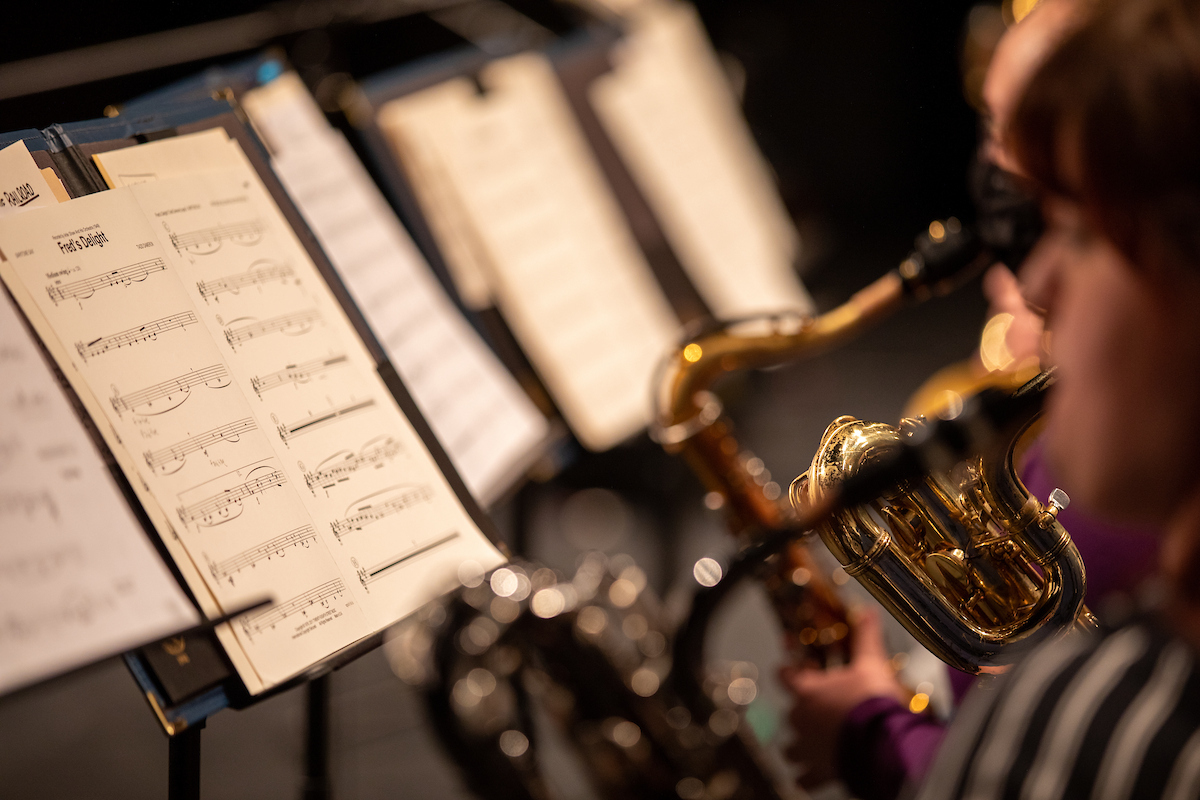 Musician playing a brass instrument while reading sheet music on a stand during a performance.