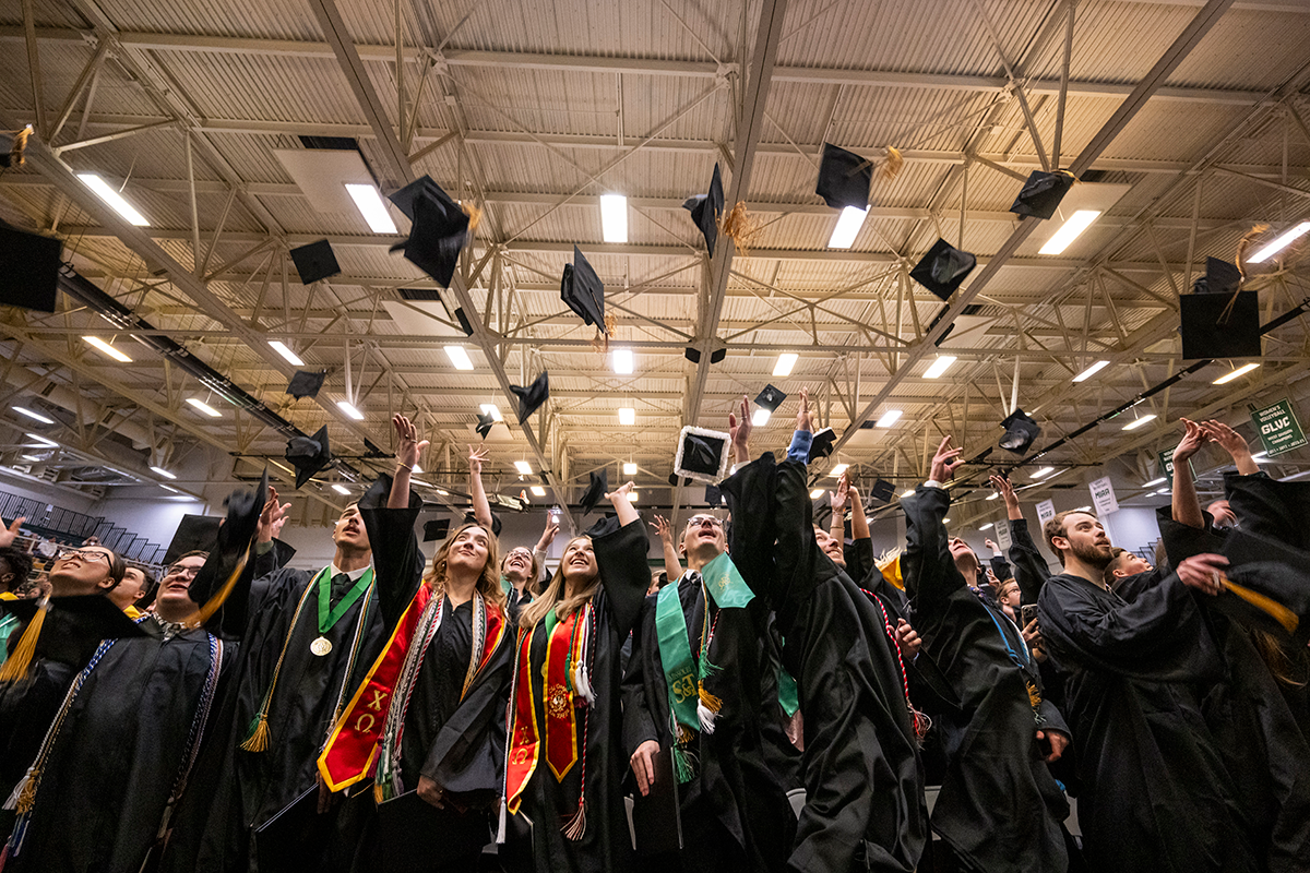 Graduates throw their caps up into the air in a gymnasium.