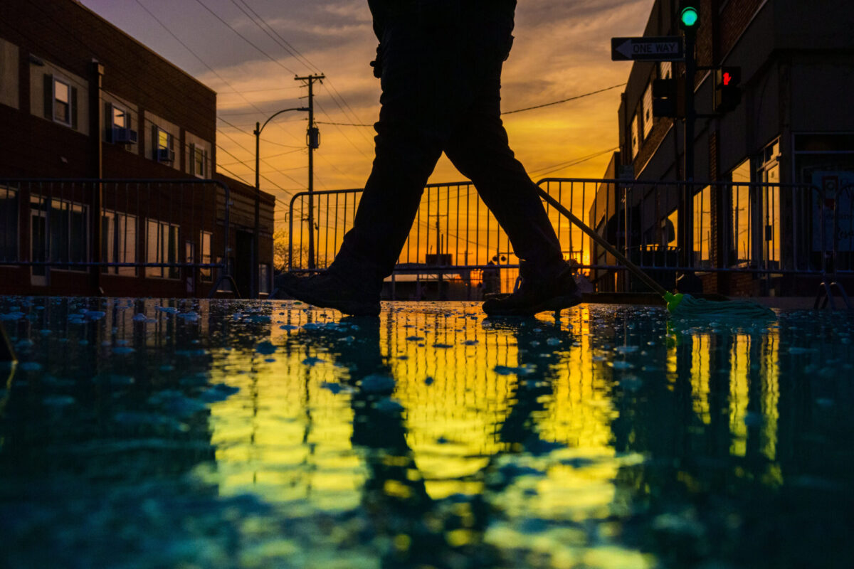 Silhouette of a person walking across Pine Street painted green, reflected in wet pavement at sunset during Missouri S&T’s St. Pat’s celebration.