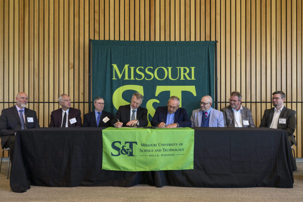 Several people seated at a table sign documents beneath a banner reading “Missouri S&T."