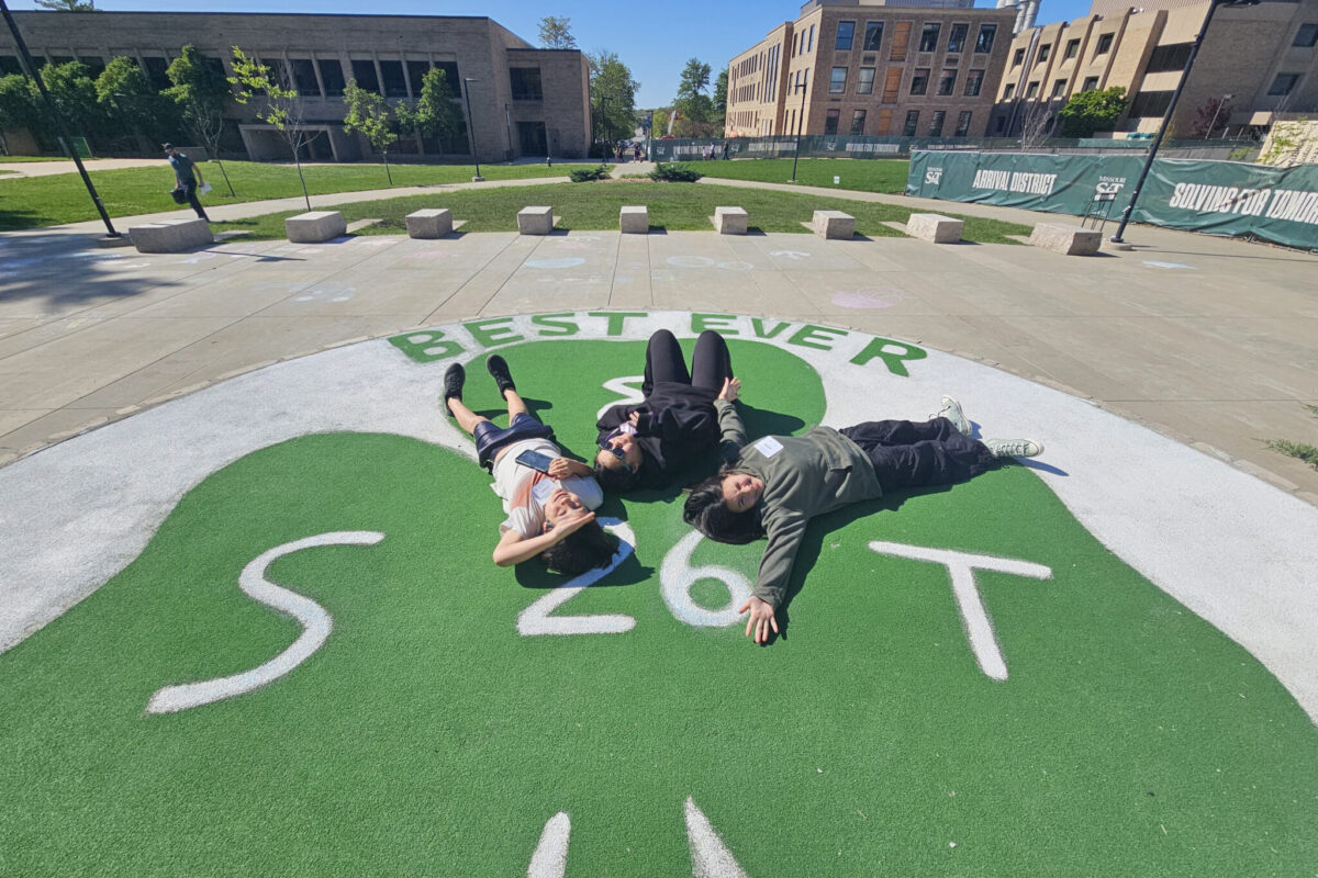 Three people lie on a green clover painted on the Puck, a circular stage located on the Missouri S&T campus.