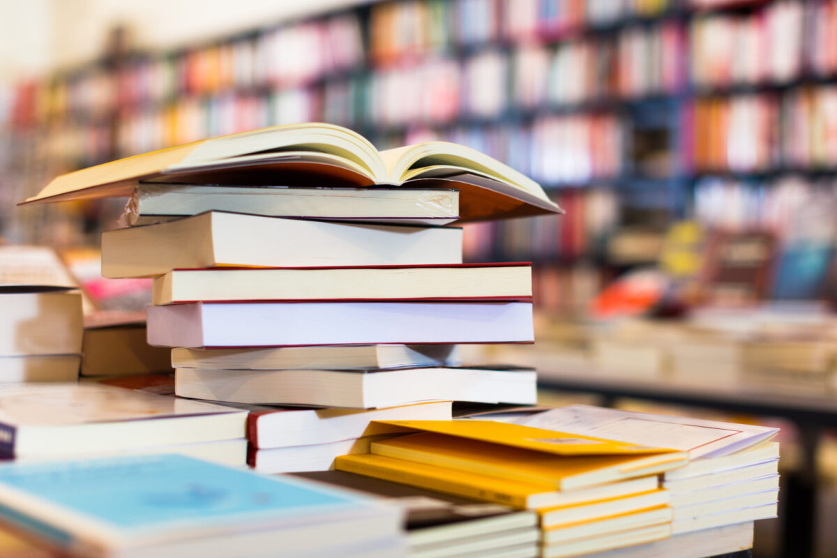 Stack of books on a table with book shelves in the background.