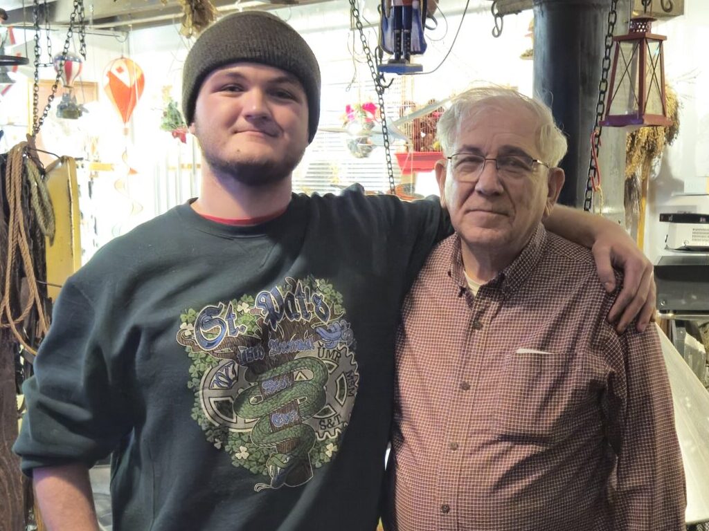 A young man poses with an older man with his arm around him.