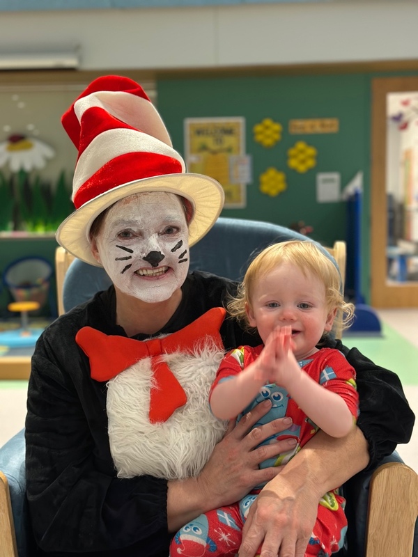 A person dressed as Cat in the Hat with face paint holds a small child.