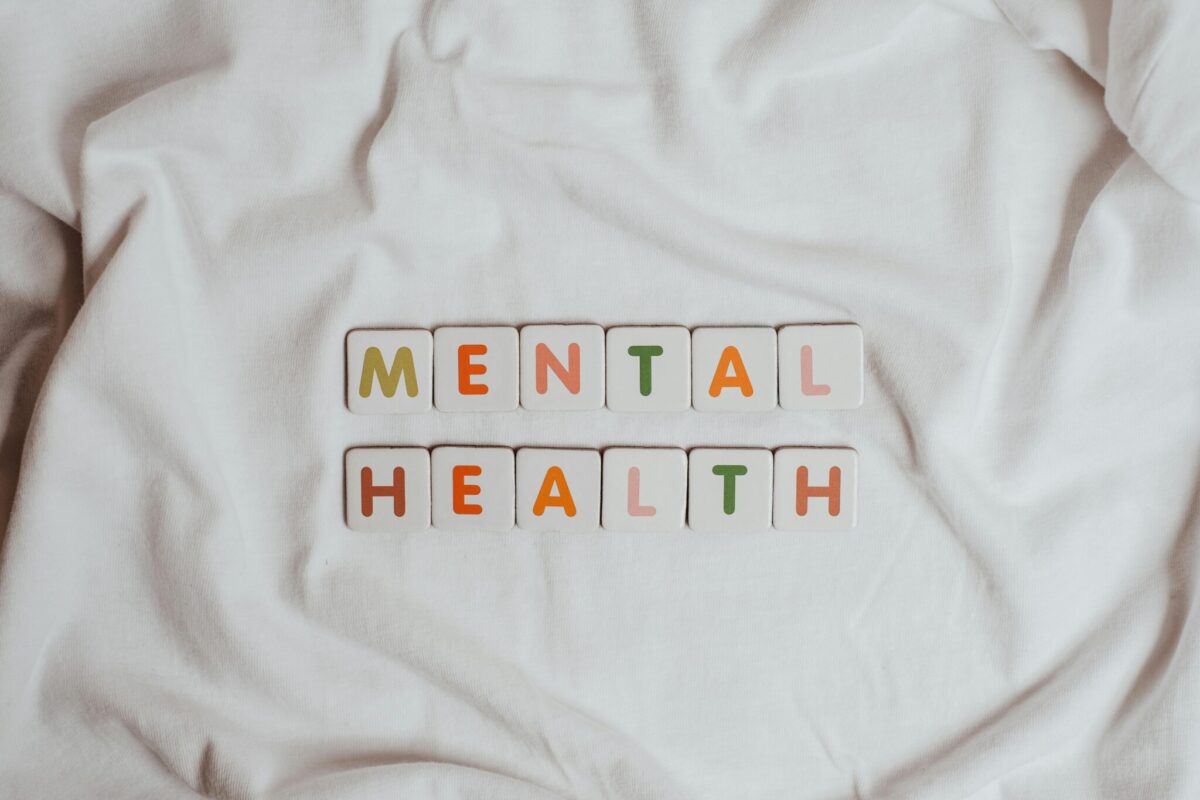 Letter tiles spelling “MENTAL HEALTH” arranged in two rows on a white, textured fabric surface.