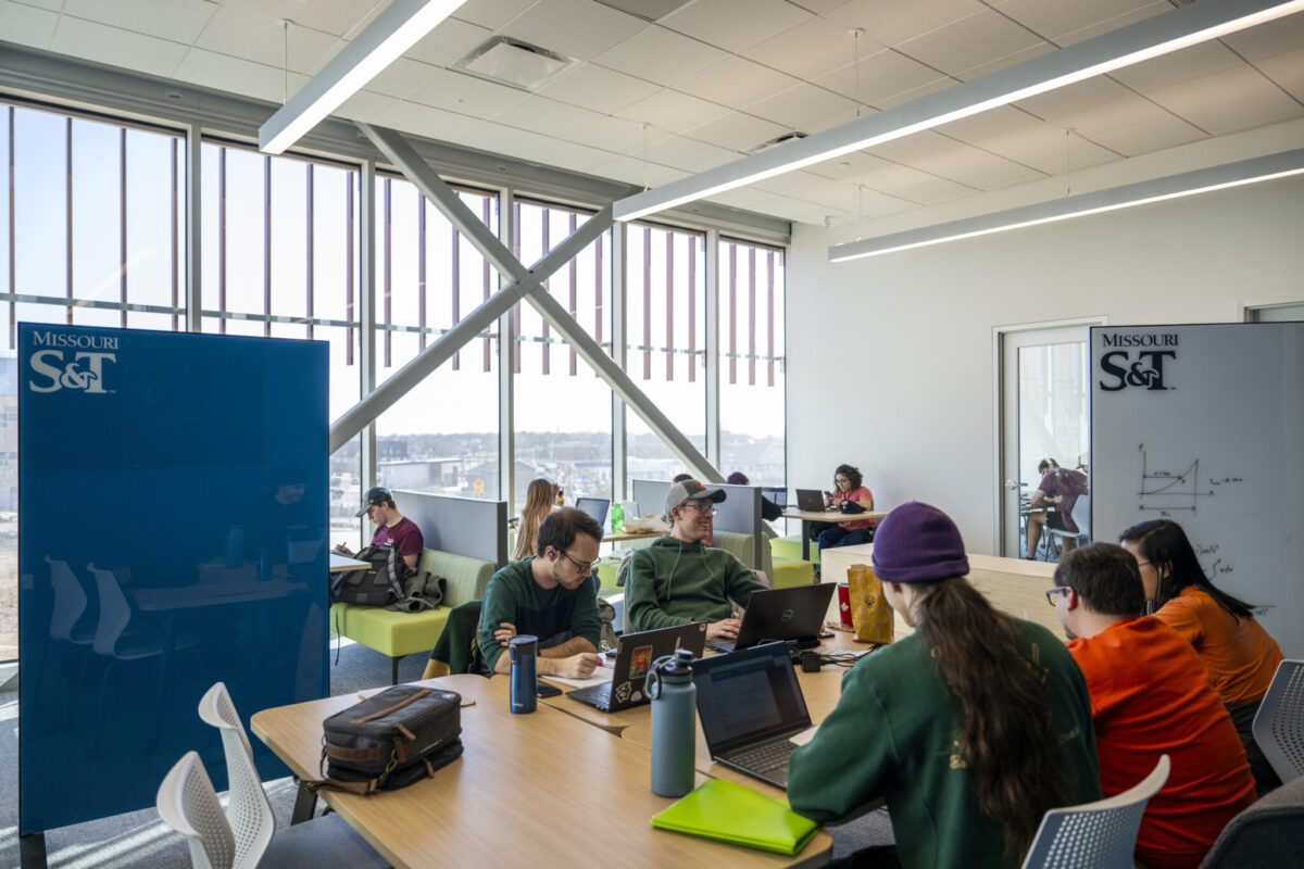 Students working on laptops together in a bright study space with large windows and “Missouri S&T” signage.