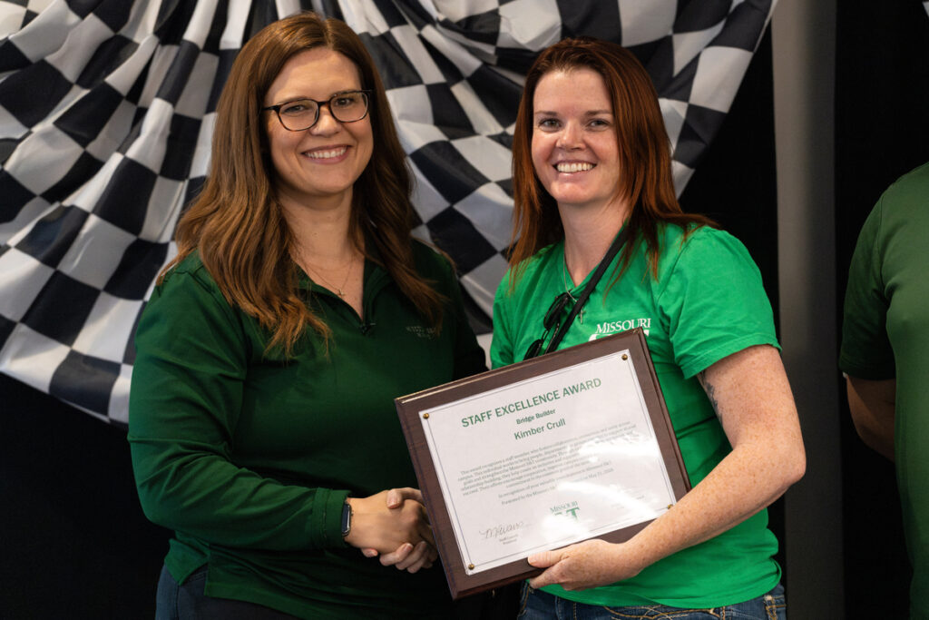 Two people on stage holding a “Staff Excellence Award” certificate at S&T’s Staff Appreciation Day event.