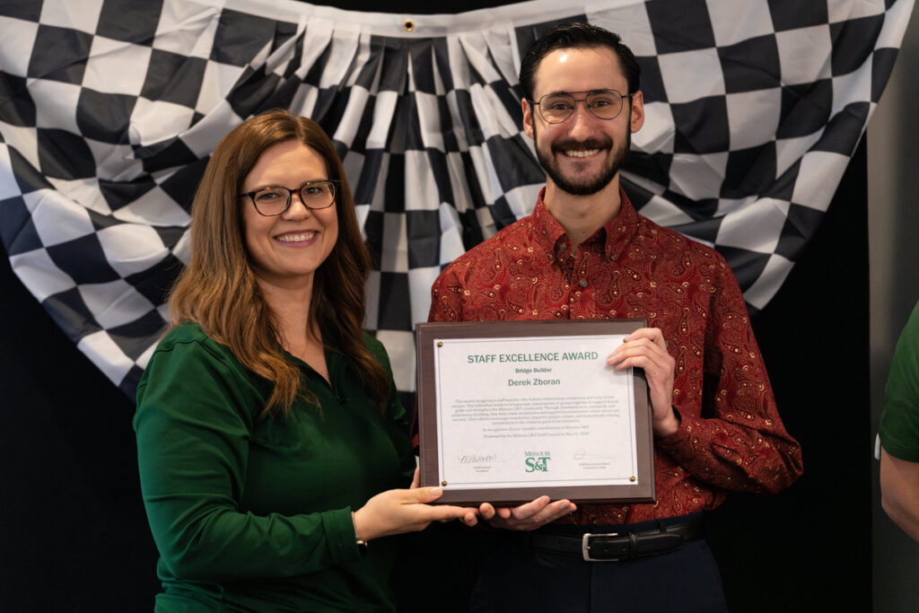 Two people on stage holding a “Staff Excellence Award” certificate at S&T’s Staff Appreciation Day event.