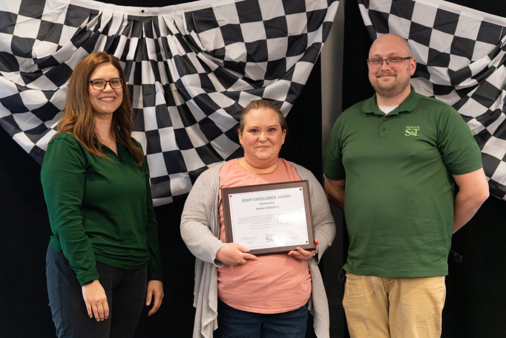 Three people on stage holding a “Staff Excellence Award” certificate at S&T’s Staff Appreciation Day event.