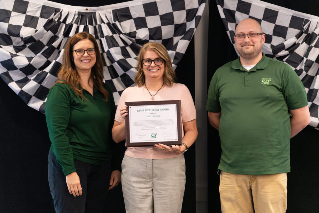 Three people on stage holding an award certificate at S&T’s Staff Appreciation Day event.