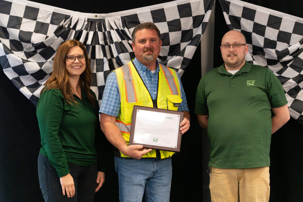 Three people on stage holding an award certificate at S&T’s Staff Appreciation Day event.