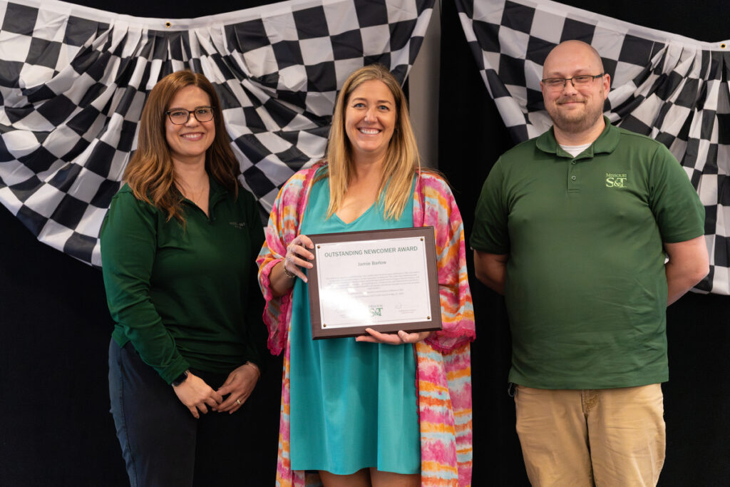 Three people on stage holding an “Outstanding Newcomer Award” certificate at S&T’s Staff Appreciation Day event.
