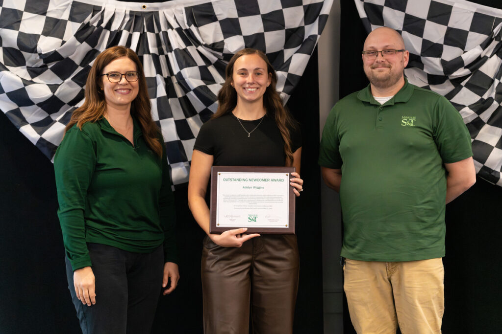Three people on stage holding an “Outstanding Newcomer Award” certificate at S&T’s Staff Appreciation Day event.